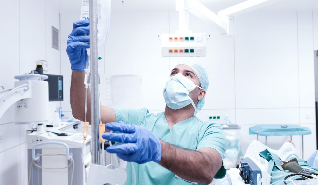 Ein Arzt in der Anästhesie hängt bei einem Patienten im OP eine Infusion an.