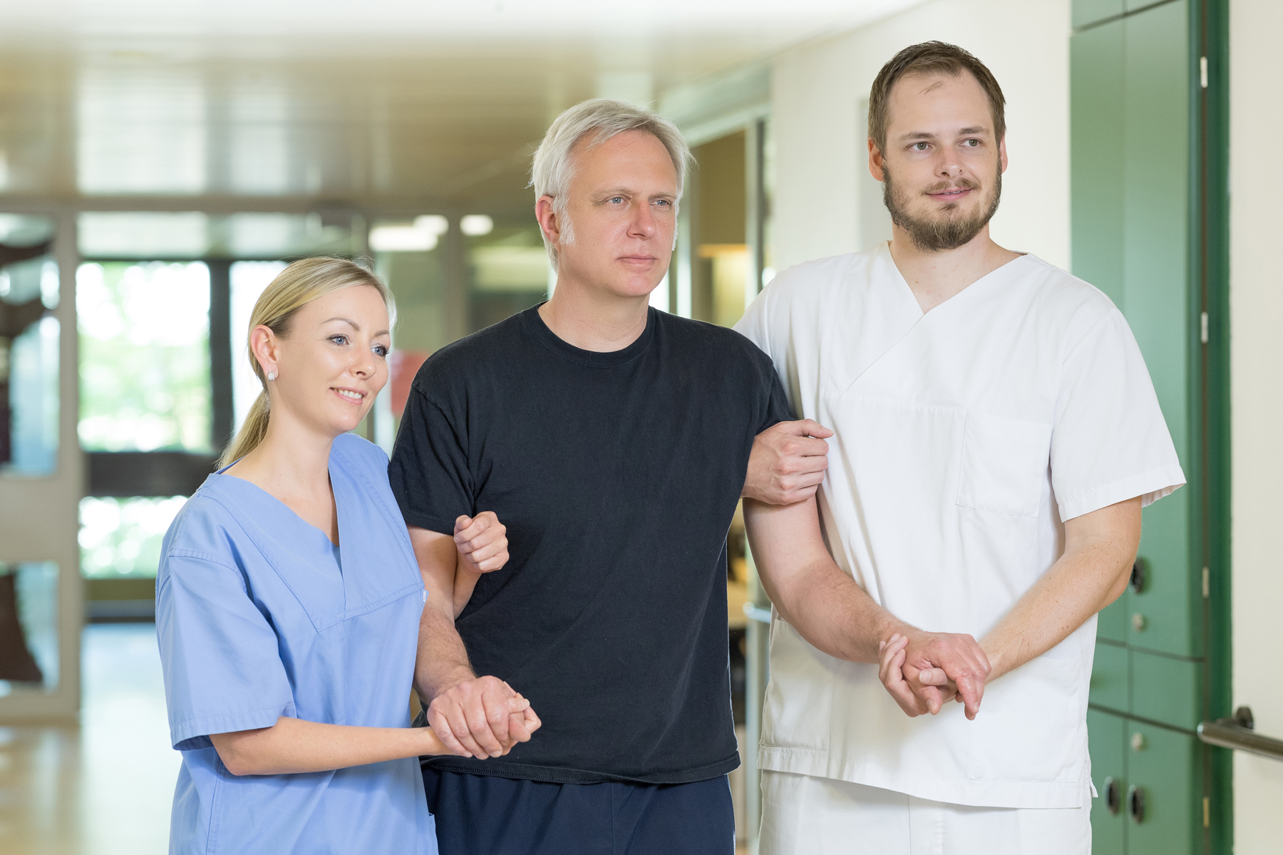 Zwei Pflegekräfte des Klinikums Ingolstadt stützen einen älteren Herren beim Gehen.
