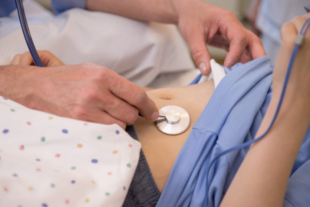 Ein Arzt hört mit einem Stethoskop den Bauch eines Jungen ab
