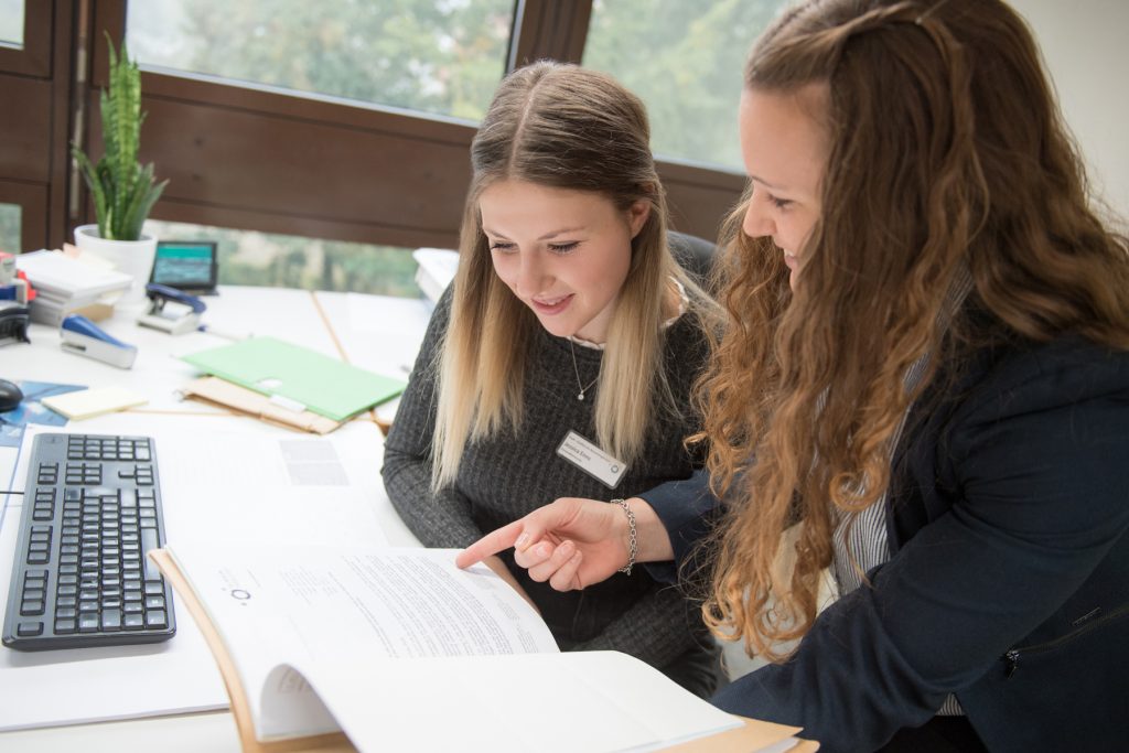 Eine Ausbilderin erklärt einer Auszubildenden die Personalakten.
